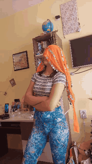 a woman wearing an orange head scarf stands with her arms crossed in front of a globe