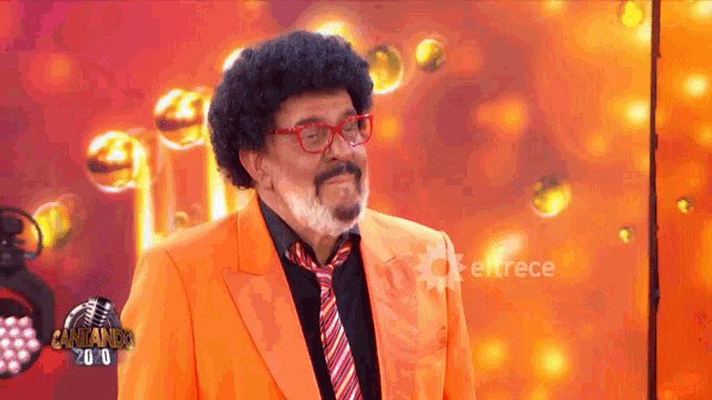 a man in an orange suit and tie is standing in front of a sign that says cantando 2.0