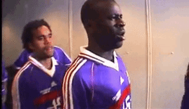 a man in a purple jersey with the number 5 on it stands next to another man