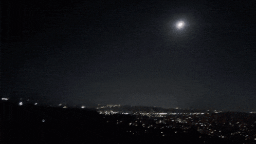 a full moon shines brightly in the night sky over a city