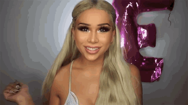 a woman with long blonde hair is smiling in front of a pink balloon that says e.