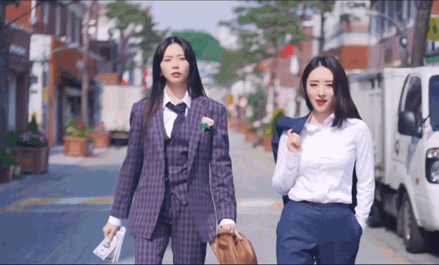 two women wearing suits and ties are walking down the street