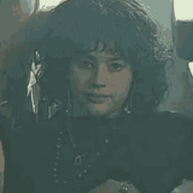 a close up of a woman with curly hair wearing a black shirt and necklace .