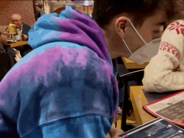 a man wearing a mask and a tie dye hoodie is sitting at a table