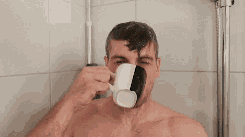 a shirtless man is taking a shower while drinking from a cup .