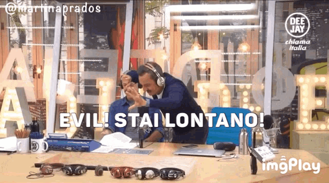 a man wearing headphones says " evil stai lontano " while another man looks on