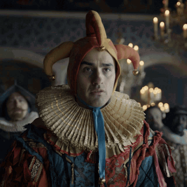 a man wearing a jester hat and collar looks at the camera