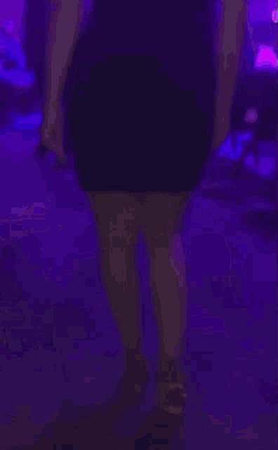 a woman in a black dress is dancing in a club with purple lights
