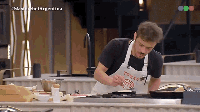 a man wearing an apron that says tomas is cooking on a stove