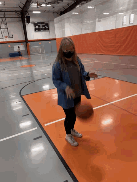 a woman wearing a mask is dribbling a basketball on an orange court