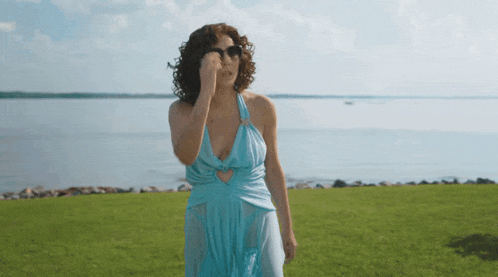 a woman in a blue dress is standing in a field near the water