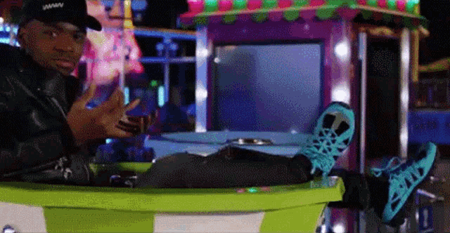 a man wearing a black hat and blue shoes is sitting on a green carousel at a carnival .