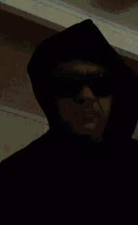 a man wearing sunglasses and a black mask with the letter s on his face is smoking a cigarette