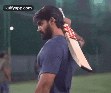a man in a blue shirt is holding a cricket bat in his hands .