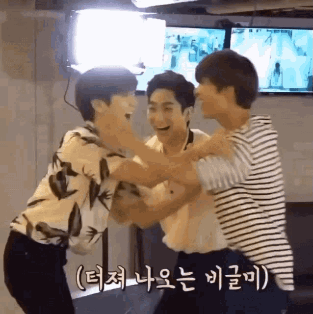 a group of young men are hugging each other in front of a television with korean writing on it