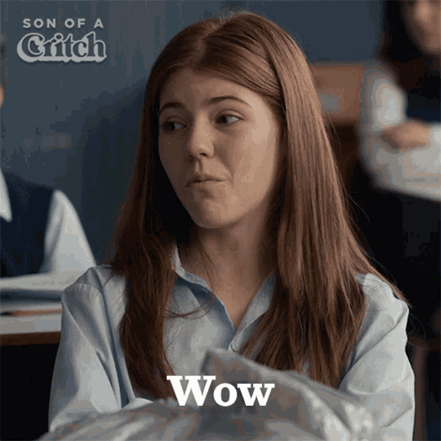 a girl with red hair is sitting in a classroom and the word wow is on the bottom right