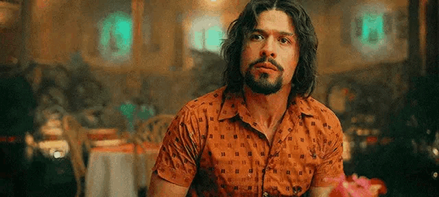 a man with long hair and a beard is sitting in a restaurant looking at the camera .