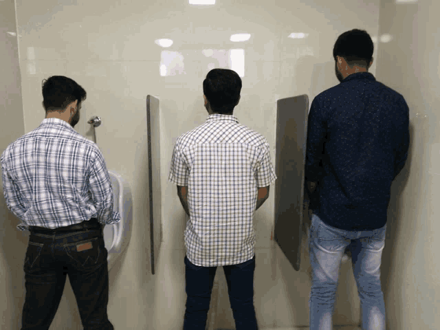 three men are urinating in a public restroom