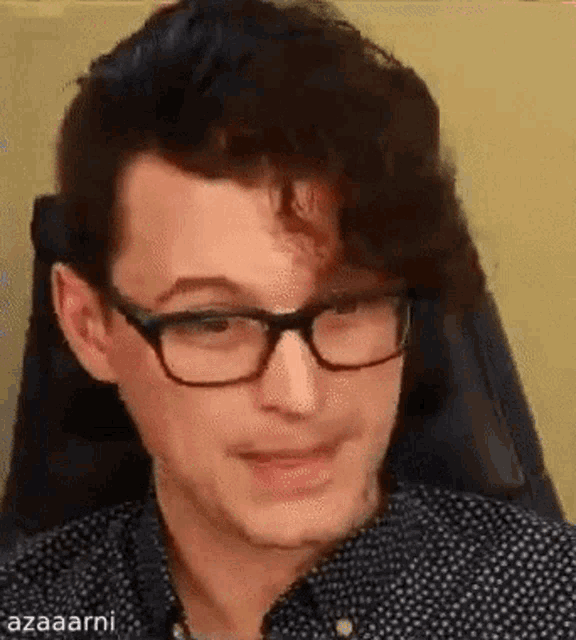 a man wearing glasses and a black and white polka dot shirt is sitting in a chair .