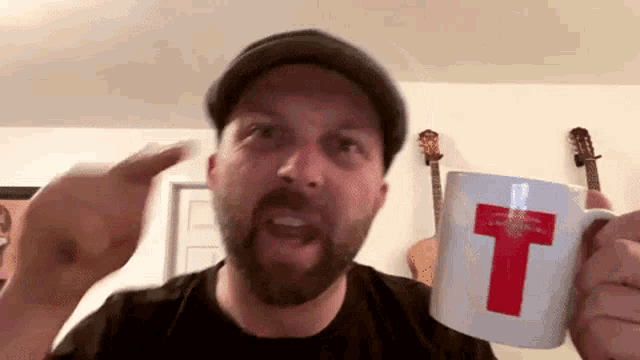 a man with a beard is holding a coffee mug with a red cross on it