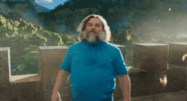 a man with a beard wearing a blue shirt stands in front of a mountain