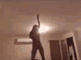 a woman is dancing in a room with a light on the ceiling .