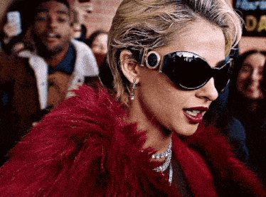 a woman wearing sunglasses and a red fur coat has the number 100 on her sunglasses