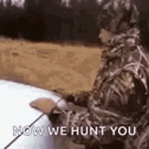 a man in a camouflage suit is standing next to a car holding a fishing rod and a fishing pole .