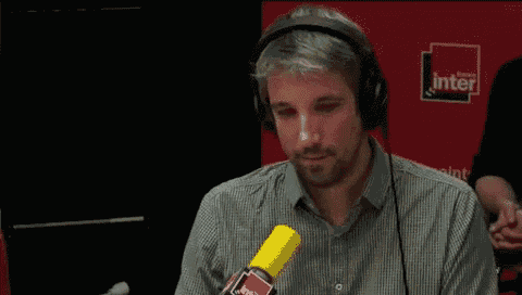 a man wearing headphones talks into a microphone in front of a red wall that says inter