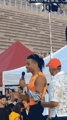 a man in an orange shirt is holding a microphone and talking to a man in an orange hat