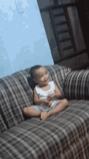 a baby is sitting on a couch with his legs crossed and smiling
