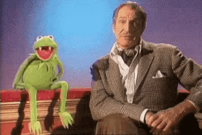 a man in a suit is sitting next to a kermit the frog puppet on a book .