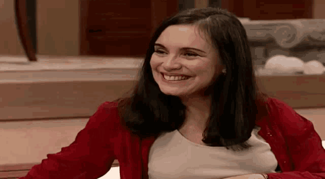 a woman is wearing a red cardigan and smiling while sitting on a couch .