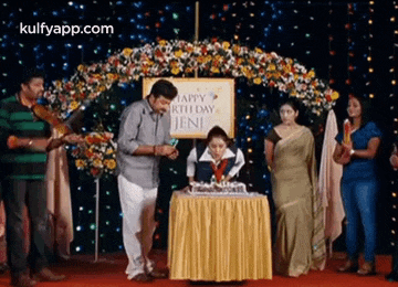a group of people standing around a table with a sign that says happy birthday jeni on it