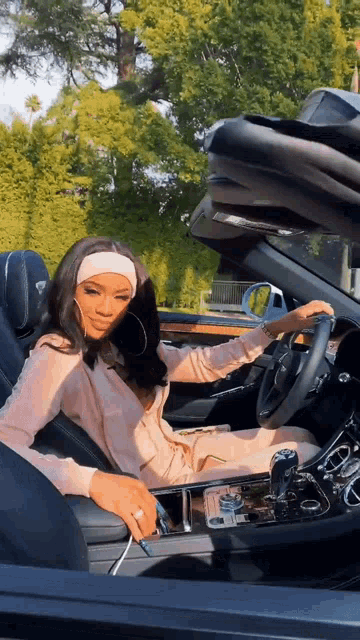 a woman is sitting in the driver 's seat of a convertible .
