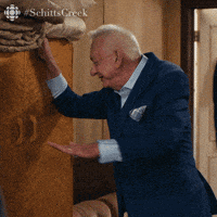 a man in a suit is standing in front of a wall with #schitts creek written on the bottom