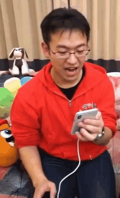 a man wearing glasses and a red hoodie is holding a cell phone