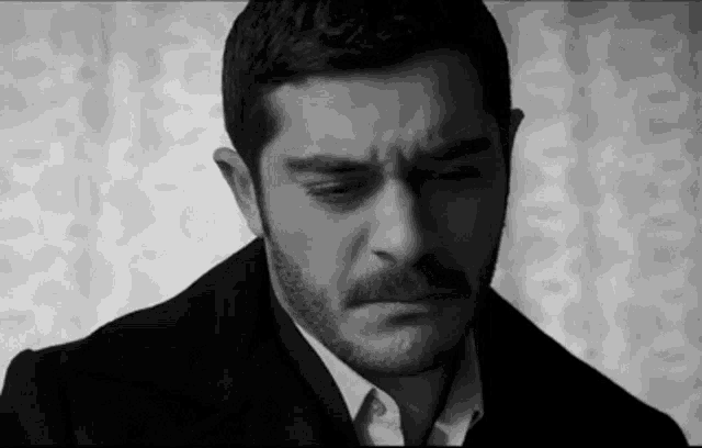a black and white photo of a man with a beard making a sad face .
