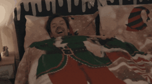 a man in a christmas sweater is laying in a bed