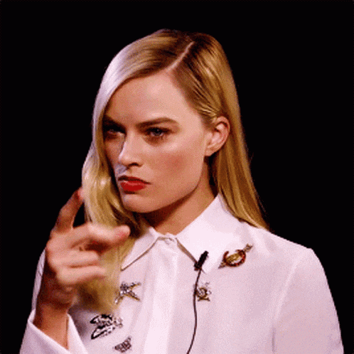 a woman in a white shirt is pointing her finger at the camera