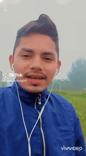 a man wearing ear buds and a blue jacket has a tiktok sticker on his face