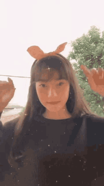 a girl wearing a headband with a bow on it is waving at the camera .