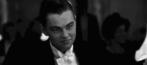 a man in a tuxedo and bow tie is holding a glass of wine in his hand .