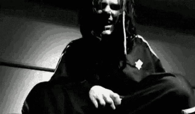a black and white photo of a man with dreadlocks sitting down .