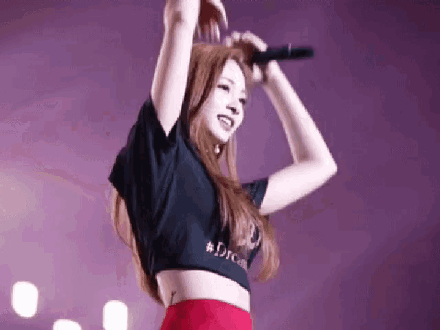 a woman is singing into a microphone while wearing a black crop top that says dream