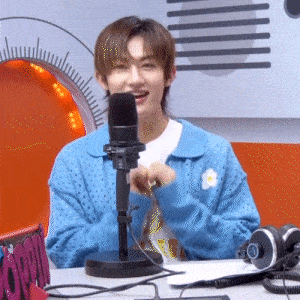 a young man in a blue sweater is sitting in front of a microphone