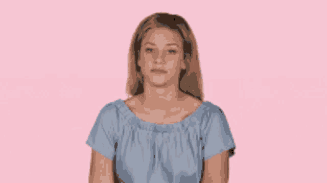 a woman wearing a blue off the shoulder top is sitting on a pink background