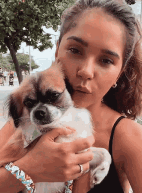 a woman in a black tank top is holding a small brown and white dog