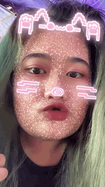a girl with green hair is wearing a face mask with emojis on her face and the letters a and b on her forehead