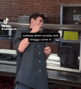 a man covering his face while standing in front of a subway